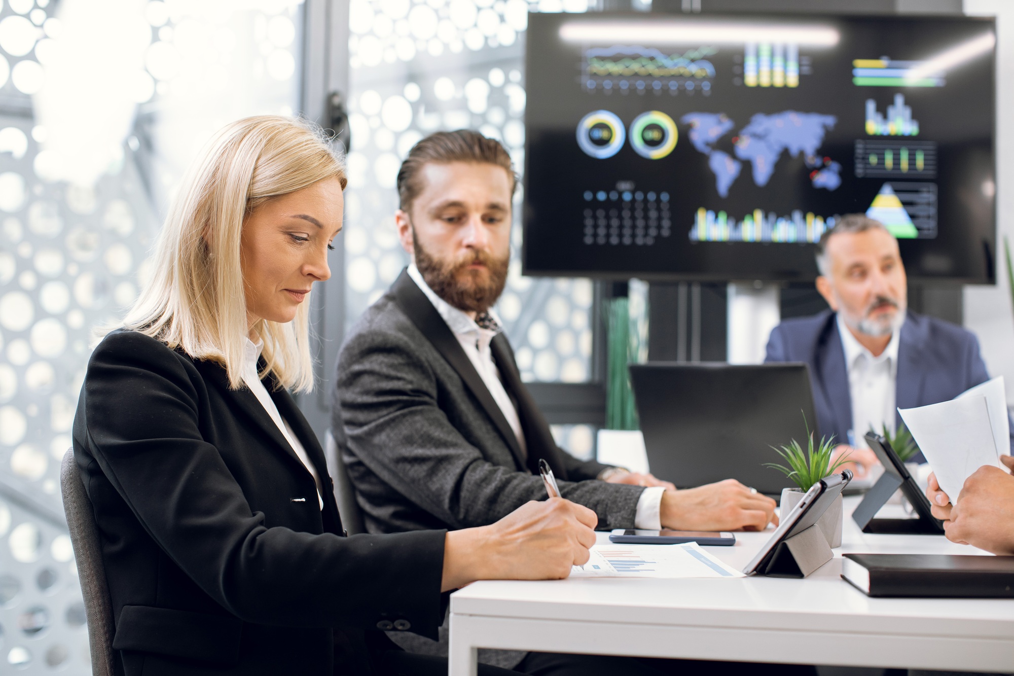Smart focused businesspeople having meeting in boardroom at office in front of plasma TV screen with